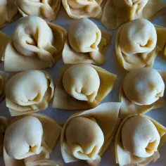 Surowe, ręcznie robione tortellini ułożone na blacie.