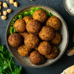 Chrupiące kulki falafel na talerzu, obok sosu i pieczywa. Falafel co to? To pyszna przekąska z ciecierzycy.
