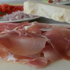 Cienkie plastry szynki crudo, obok kawałek parmezanu i talerz z posiekanymi warzywami. Idealne na przekąskę.