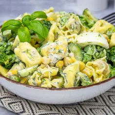 Sałatka z tortellini, brokułów, kukurydzy, ogórka i jajka w kremowym sosie, udekorowana bazylią.