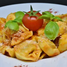 Tortellini z sosem pomidorowym, posypane parmezanem, udekorowane pomidorkiem i bazylią.