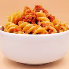 Miseczka pełna makaronu fusilli z aromatycznym sosem, w którym dominują nuty pesto i słodycz suszonych pomidorów.