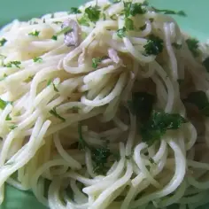 Pyszny makaron spaghetti z delikatnym sosem i posiekaną natką pietruszki, podany na zielonym talerzu.