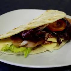 Pyszna piadina z szynką, serem, sałatą, pomidorem i cykorią na białym talerzu.
