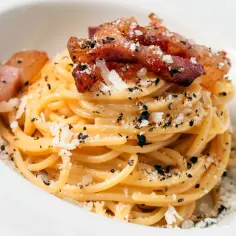 Spaghetti carbonara z chrupiącym guanciale, posypane parmezanem i czarnym pieprzem. To właśnie guanciale nadaje jej autentyczny smak.