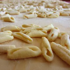 Świeży, swojski makaron przepis na domowe gnocchi. Wiele małych, zakręconych kluseczek ułożonych na blacie posypanym mąką.