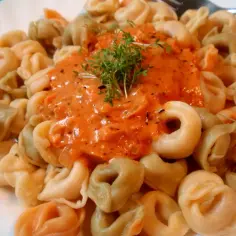 Tortellini w kremowym sosie pomidorowym, udekorowane świeżymi ziołami.