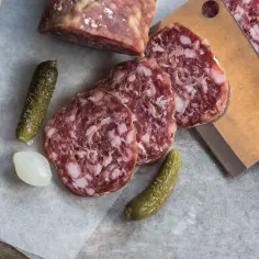 Kawałki aromatycznego salami napoli, ogórki konserwowe, cebulka i gałązka lawendy na papierze.
