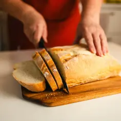 Ręce kroją świeży, złocisty bochenek chleba na desce. Pachnący, chrupiący wypiek czeka na kanapki.