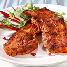 Dwa kawałki grillowanego boczku, idealnie doprawione marynatą do boczku na grilla, podane z papryczkami chili i ziołami.