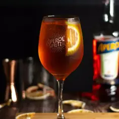 Orzeźwiający Aperol Spritz, jeden z najlepszych drinków, z plastrem pomarańczy. Obok butelka Aperolu i inne akcesoria barmańskie.