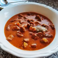 Gulasz z łopatki wieprzowej w sosie własnym, aromatyczny i sycący, podany w białej misce.