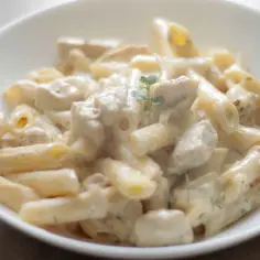 Penne z kurczakiem w kremowym sosie śmietanowym, udekorowane gałązką ziół. Pyszne danie gotowe do podania.