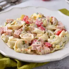 Sałatka z tortellini, szynką, pomidorkami i ogórkiem konserwowym w kremowym sosie.