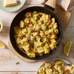 Tortellini z mięsem w kremowym sosie, posypane ziołami i boczkiem, podane z cytryną.