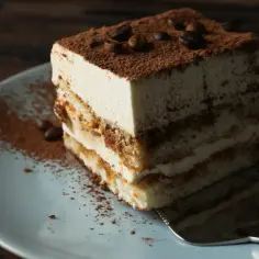 Kawałek tiramisu na talerzu, posypany kakao i ziarnami kawy.