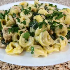 Tortellini ze szpinakiem i kurczakiem w kremowym sosie, posypane natką pietruszki.