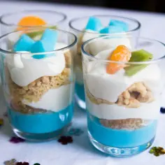 Pyszny deser z mascarpone i galaretką w pucharkach, udekorowany owocami i kostkami galaretki.