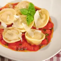 Tortellini z prosciutto w sosie pomidorowym, posypane parmezanem i udekorowane bazylią.