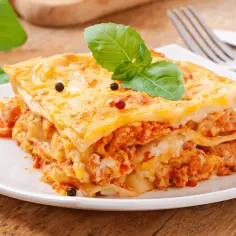 Pyszna, warstwowa lasagne z mięsem mielonym, udekorowana listkiem bazylii i pieprzem. Idealna na prosty obiad.