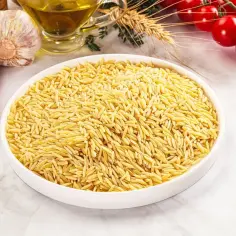 Miseczka pełna makaronu w kształcie ryżu, obok czosnek, papryczki chili, pomidorki i oliwa.