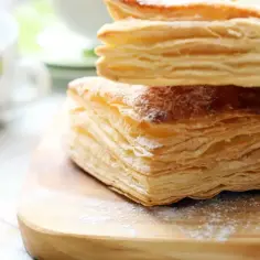 Stos warstw ciasta francuskiego, idealny do nauki, jak zrobić ciasto francuskie. Posypane cukrem pudrem, na drewnianej desce.