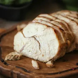 Soczysty indyk z airfryer, pokrojony w plastry, leży na drewnianej desce z pieprzem i czosnkiem.
