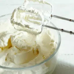 Mieszadła miksera ubijają puszysty, prosty krem z mascarpone bez śmietany w szklanej misce.