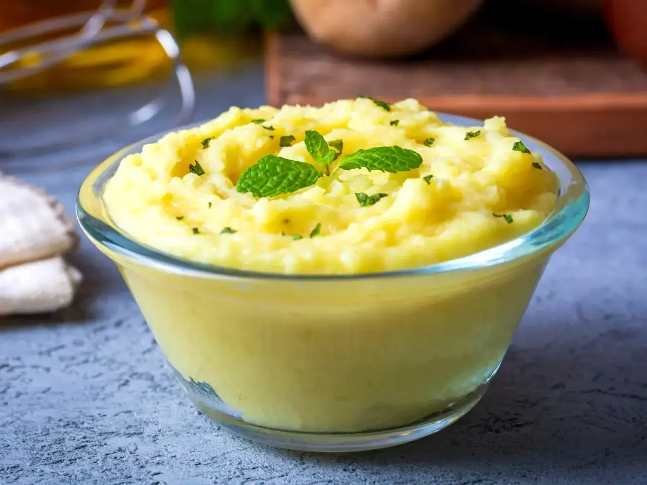 Puszyste, złociste puree ziemniaczane w szklanej misce, udekorowane listkami mięty. Idealne, gdy zastanawiasz się, jak zrobić puree.