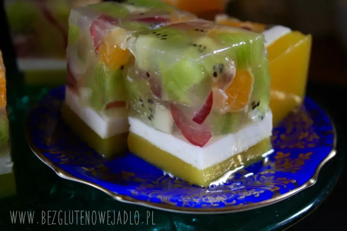 Kolorowe galaretki z owocami, w tym kiwi i mandarynki, na niebieskim talerzyku. To pyszny deser na bazie agaru.
