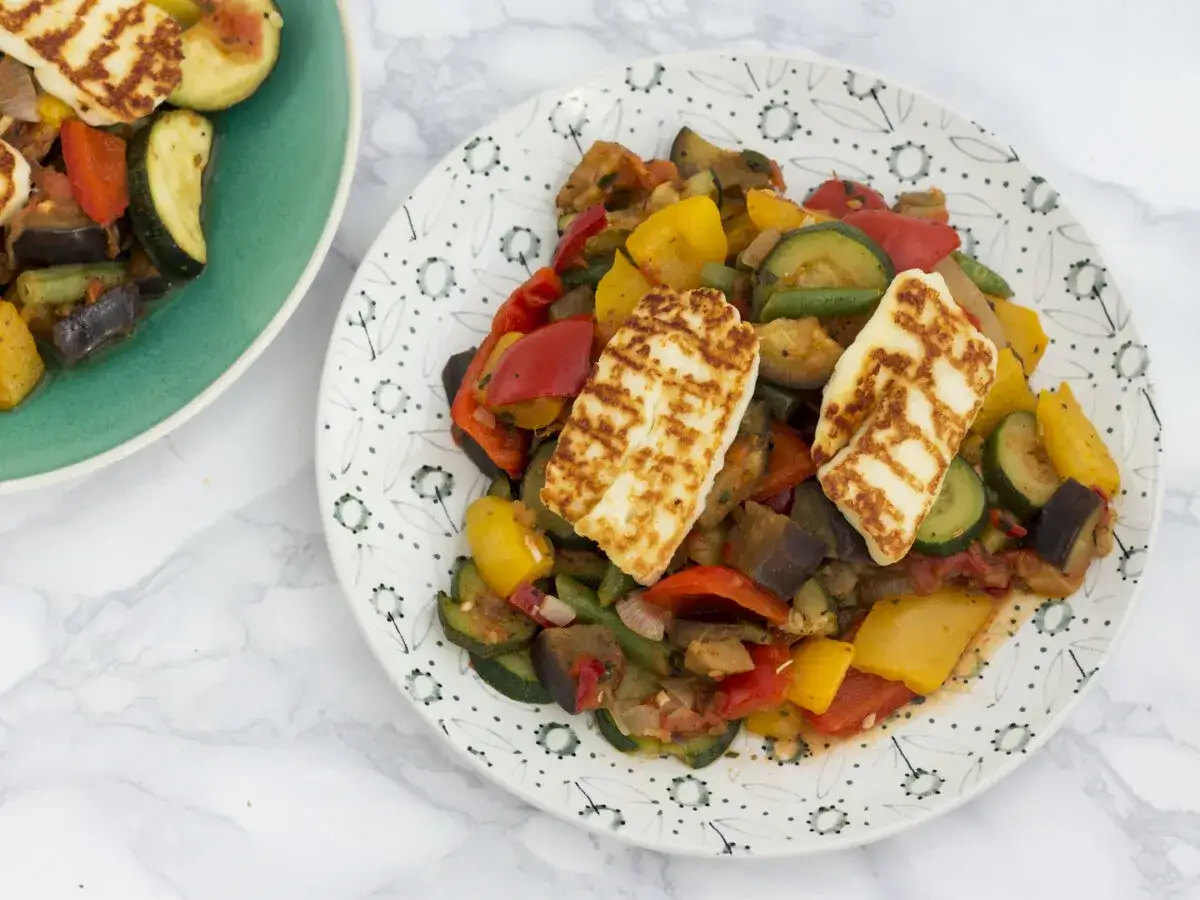 Dwa talerze z warzywami z grilla i grillowanym serem halloumi. Kolorowe papryki, cukinia, bakłażan i fasolka szparagowa tworzą apetyczną kompozycję.