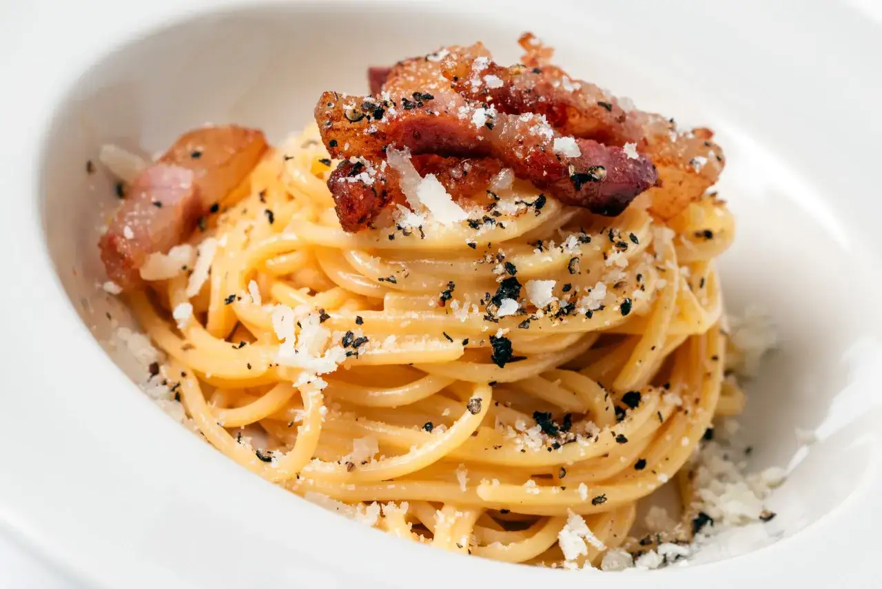 Spaghetti carbonara z chrupiącym guanciale, posypane parmezanem i czarnym pieprzem. To właśnie guanciale co to jest, sekretny składnik tej potrawy.