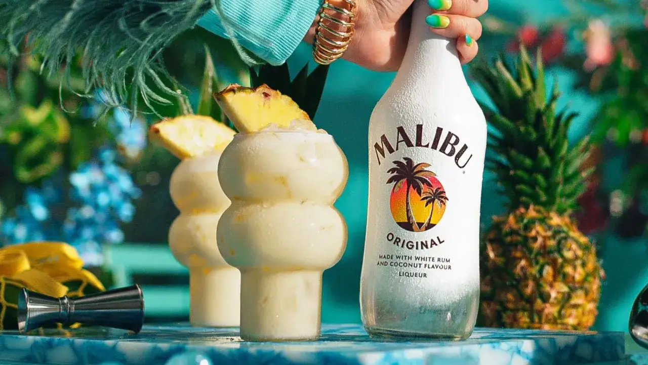 Pyszny przepis na Pina Coladę z Malibu. Kremowy koktajl z ananasem i lodem, obok butelka Malibu i świeży ananas.