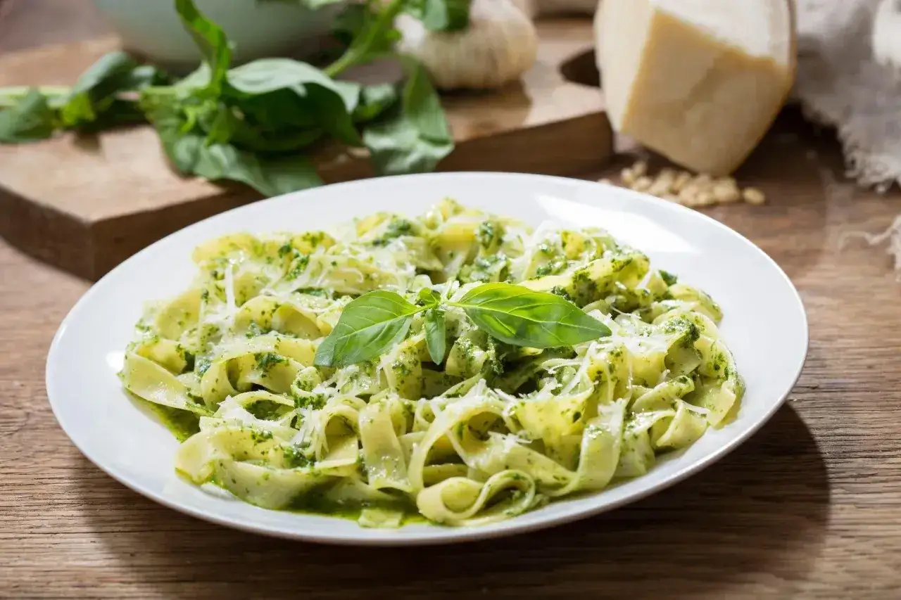 Talerz tagliatelle z aromatycznym pesto z rukoli, posypany parmezanem i udekorowany listkiem bazylii.