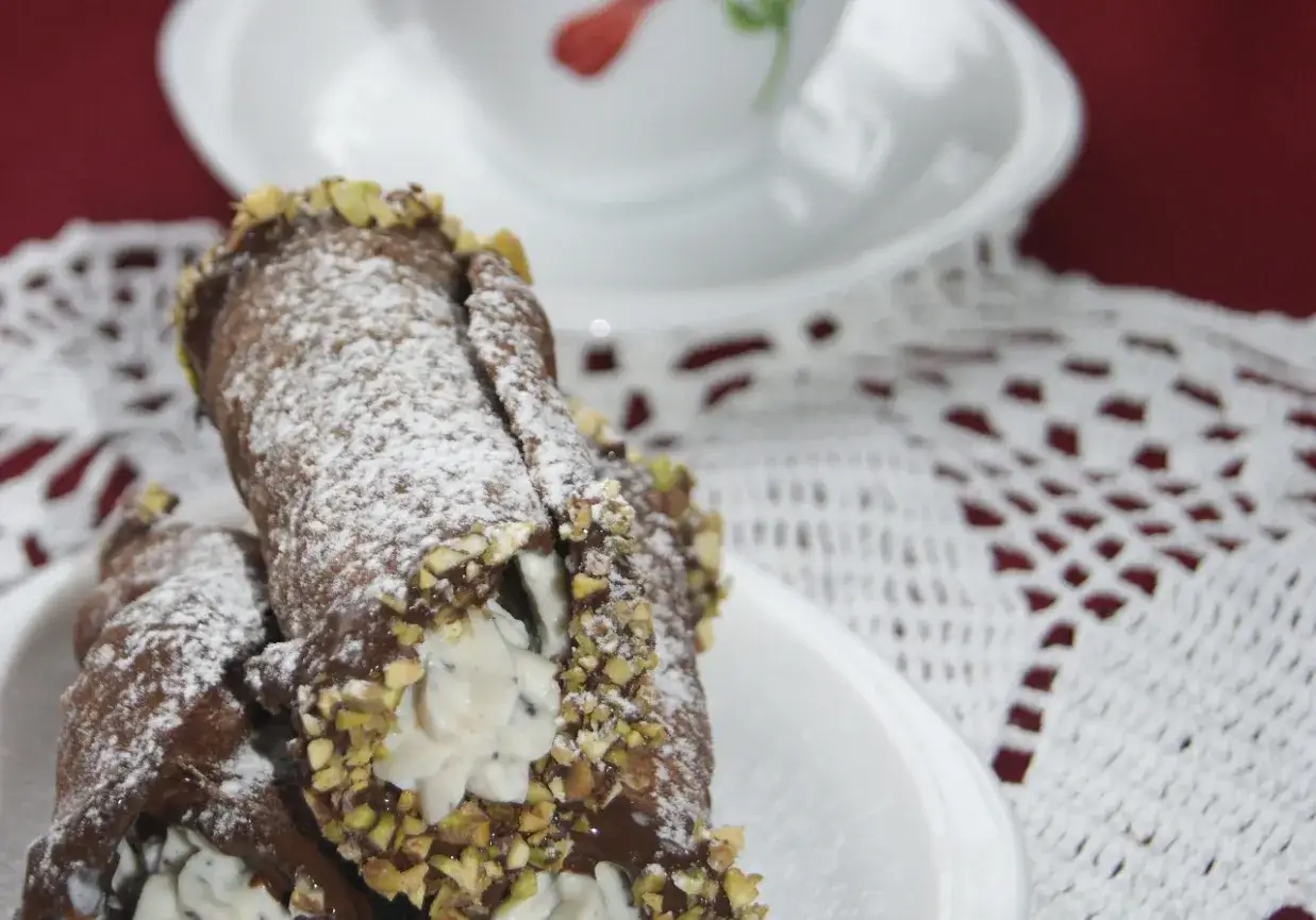 Dwa pyszne cannoli, posypane cukrem pudrem i pistacjami, czekają na talerzyku.