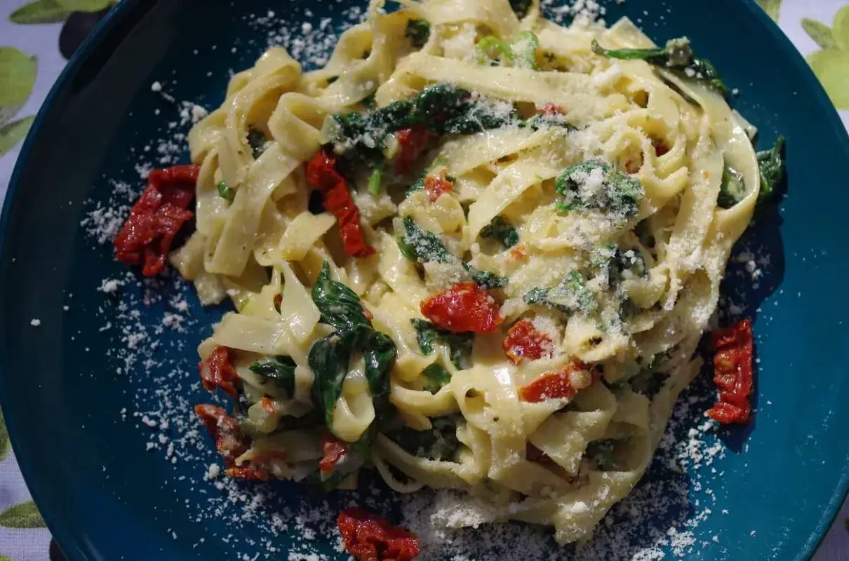 Pyszny makaron ze szpinakiem i pomidorami, posypany parmezanem, na talerzu.