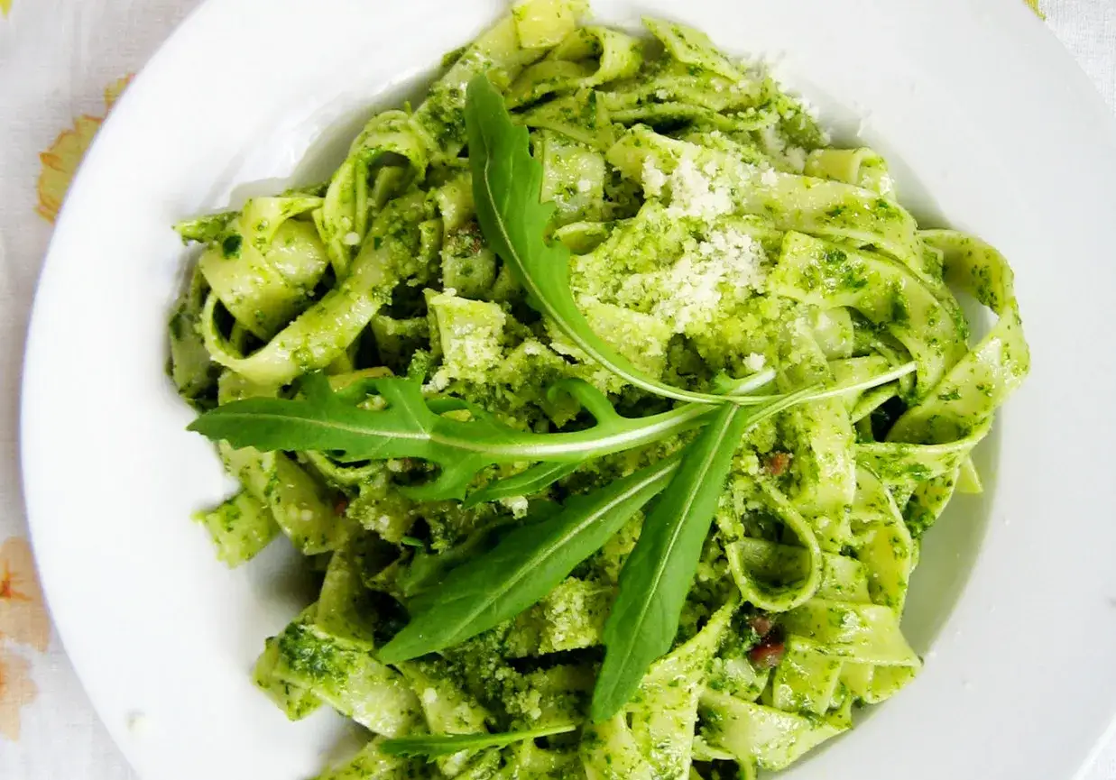 Pappardelle z intensywnym pesto ze szpinaku, posypane parmezanem i udekorowane rukolą.