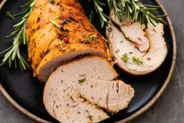 Soczyste, pieczone filet z indyka z ziołami i pieprzem, pokrojone w plastry, podane na czarnym talerzu z gałązkami rozmarynu.