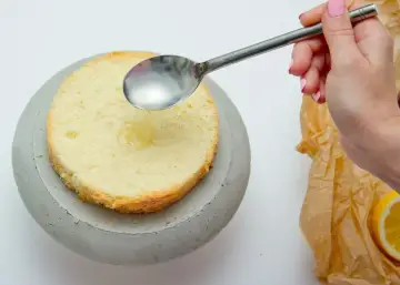 Dłoń z łyżką polewa biszkopt syropem. To klucz do pytania, czym nasączyć biszkopt, by był wilgotny i pyszny.