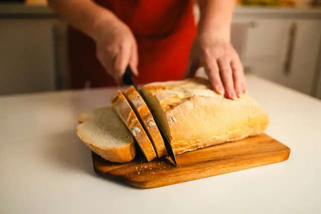 Ręce kroją świeży, złocisty bochenek chleba na desce. Pachnący, chrupiący wypiek czeka na kanapki.